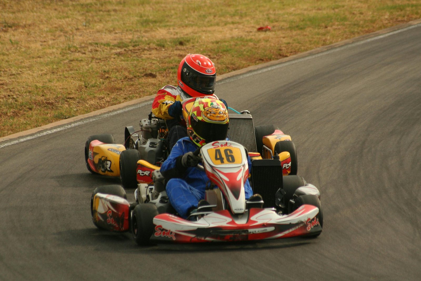 Close-up action shot of two go-kart racers competing on a curving race track.
