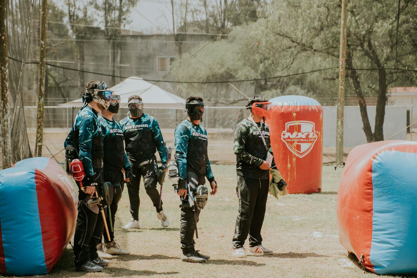 Group of paintball players strategizing in outdoor arena with gear and masks.